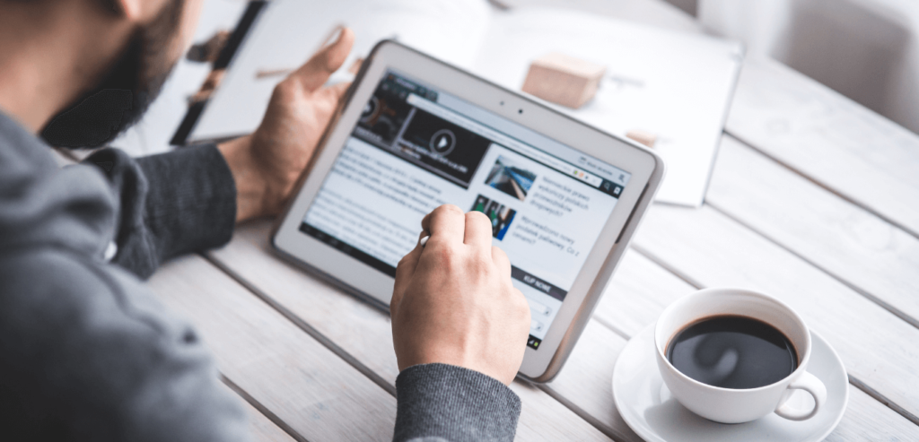 a white male sits at a table with a cup of coffee holding his ipad