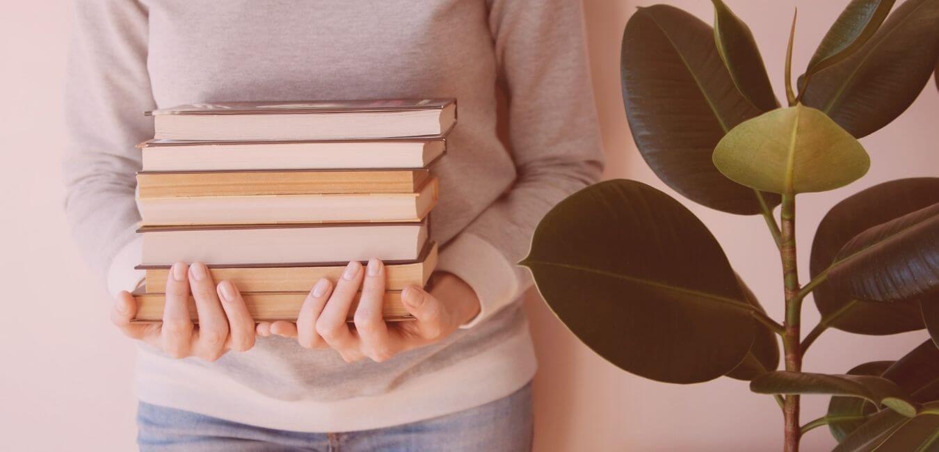 Person holding a pile of books next to a pot plant