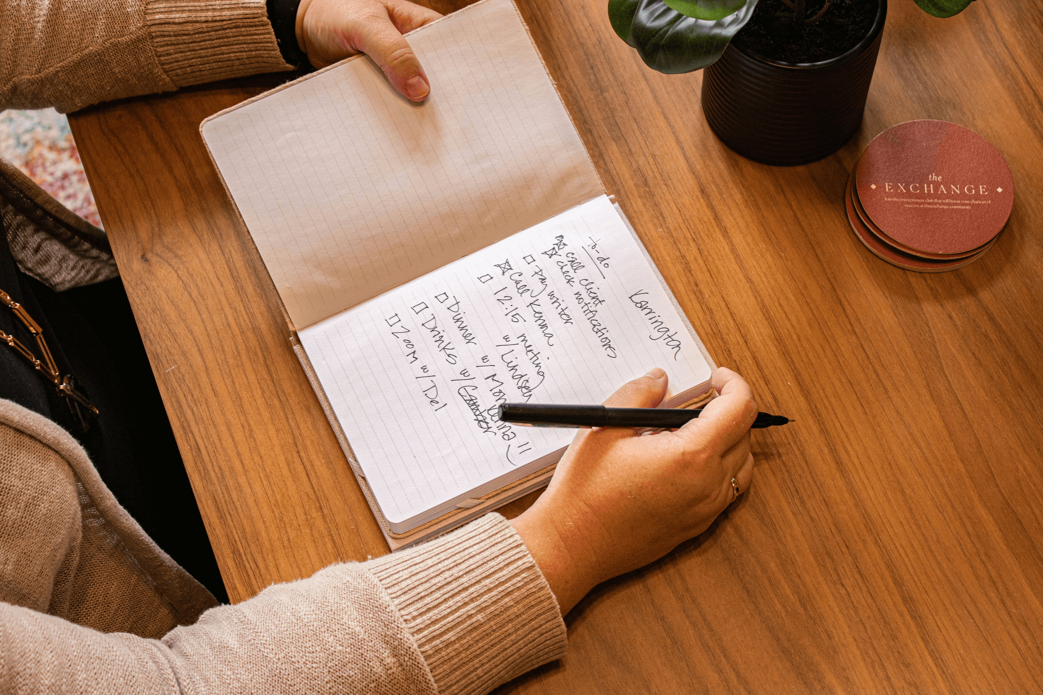 A white female is making a list in a notebook. Only her hands and arms are visible