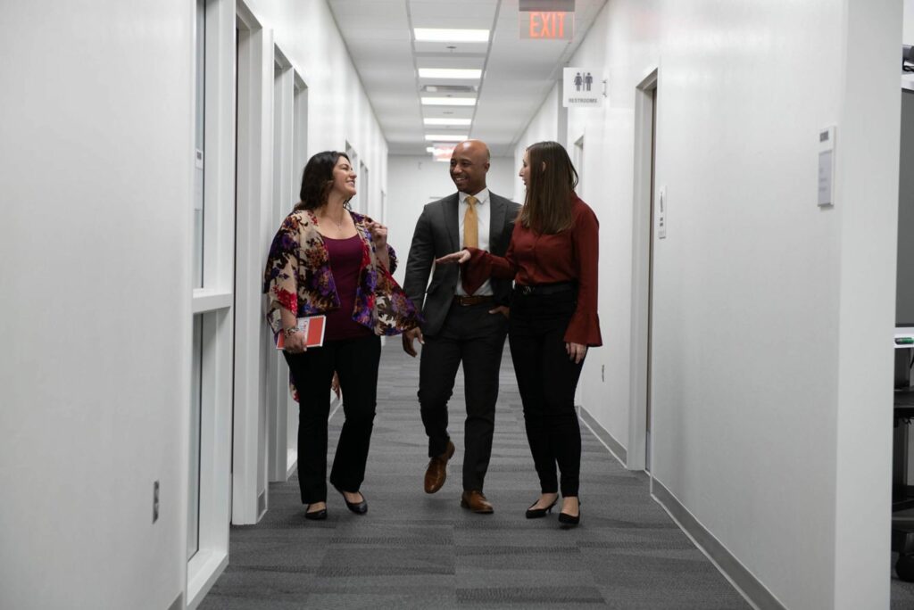 Two women and a man walking down a hall talking